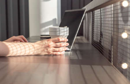 Woman hands working on laptop and holding takeaway cup. Student or freelancer sitting at table in...