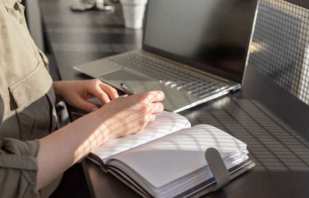 Woman hands taking notes in notebook and working on laptop. Online education and work concept....