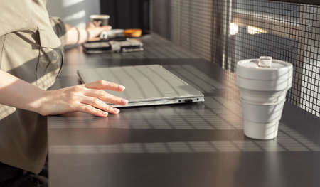 Woman sitting at cafe table with closed laptop and eco cup. Woman hand taking notepad. Work or study...