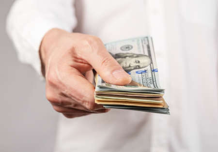 Businessman hand closeup holding US dollars stack. Finance and tax concept. Man receiving or paying...