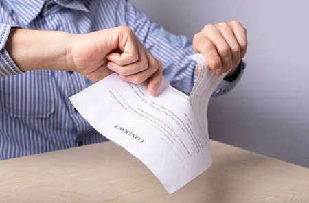 Man hands closeup tearing contract. Termination of partnership, deal concept. Man sitting at desk in office and tearing document. Worker firing. High quality photoの写真素材