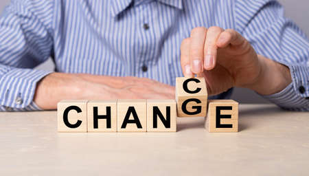 Hand flipping cube with word chance to change. Man sitting at table with wooden cubes. Personal...