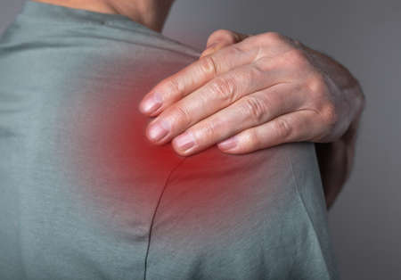 Man suffering from shoulder pain. Trigger point. Hand holding shoulder with red spot closeup. Health problems, medicine concept. High quality photoの写真素材