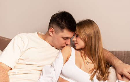 Couple sitting on couch. Handsome man kissing wife or girlfriend on shoulder. Passion, love,...