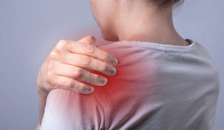Woman suffering from shoulder pain. Hand holding painful shoulder with red point closeup. Joint...