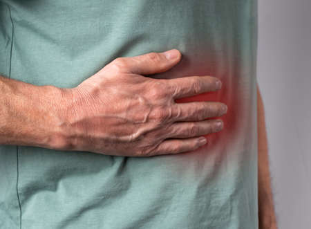 Liver pain. Man hand holding abdomen right side with red point closeup. Diseases, alcohol abuse, health care, treatment concept. High quality photoの写真素材