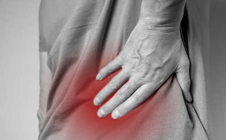 Lower back pain. Lumbago. Man hands holding red painful point closeup. Spinal injury, pinched muscles. Health problems, cure concept. High quality photoの写真素材