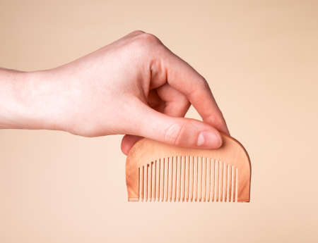 Woman hand holding wooden comb. Hair care and beauty concept. Hairbrush on beige background. High quality photoの写真素材