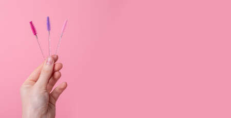 Hand with eyelash wands, brushes on pink background. Banner with copy space for text. High quality photoの写真素材