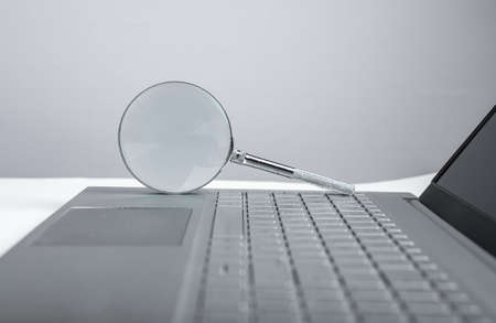 Magnifying glass on laptop keyboard. Information search concept. Audit of electronic projects, financial data. High quality photoの写真素材