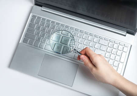 Woman hand holding magnifying glass over laptop keyboard. Information search on Internet concept. Expertise of electronic projects, financial data. High quality photoの写真素材