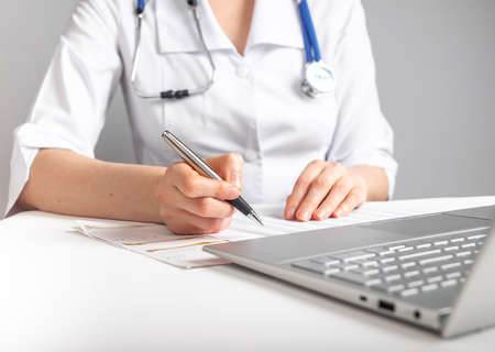Doctor with stethoscope writing with pen about patient treatment or scheduling appointments. Woman...