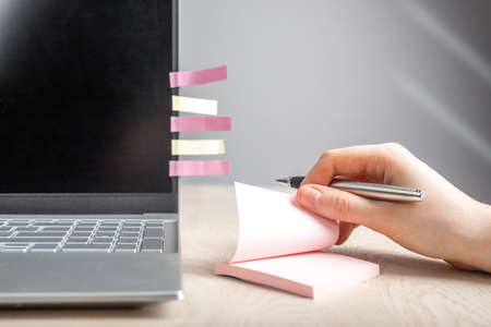 Woman hand taking memo notes at sticky papers. Female sitting at table with laptop and recording...