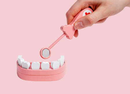 Hand with dental mirror teeth in jaw model and exploring patient oral cavity. Children game at...