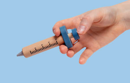 Woman hand holding wooden syringe model for medicine, vaccine, drugs injection on blue background. Health care, medical treatment concept. High quality photoの写真素材