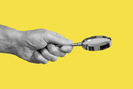 Magnifying glass in man hand on yellow background. Information search and analysis concept. Conducting check. High quality photoの写真素材