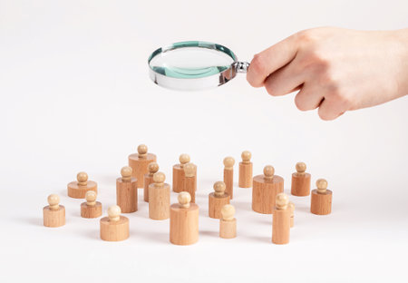 Social research. Hand with magnifying glass over Montessori knobbed cylinders like people community. Sociology concept. High quality photoの写真素材