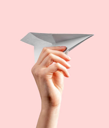 Woman hand throwing origami plane on pink background. Symbol of childhood, freedom, imagination, creativity. Paper folding art. High quality photoの写真素材