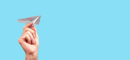 Banner with female hand throwing origami plane on turquoise background. Handmade paper aircraft. Freedom, childhood, fun concept. Place for text. High quality photoの写真素材