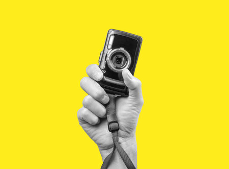 Man hand holding point and shoot camera. Black and white image on yellow background. Practical and compact digital device for taking photos in photographer arm.の写真素材