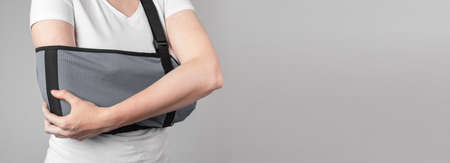 Banner with woman holding painful elbow in sling. Arm injury, overuse, inflammation consequences. Health care concept. Medical device for pain reduction and immobilizing. Copy space. photoの写真素材