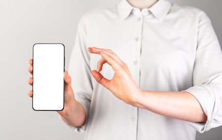 Woman holding phone mockup and showing ok gesture. Female approving, recommending mobile app to clients. Smartphone with white template. high quality photoの写真素材