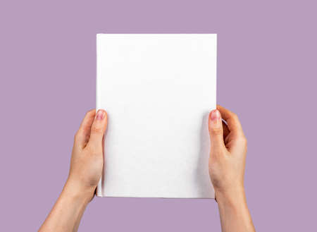 Hands holding closed book on violet background. gift. Novel, encyclopedia, cookbook, guide template with empty white cover. Education, literature concept. high quality photoの写真素材