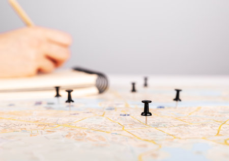 Woman planning travel itinerary. Hand taking notes in planner and marking locations to visit on map with pins. trip route organization. high quality photoの写真素材