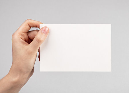 Hand holding card mockup on gray background. Empty space for congratulation, invitation, note. Paper in horizontal position. high quality photoの写真素材