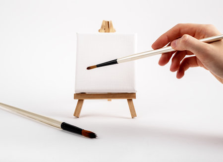 Artists hand with paintbrush painting, making stroke on blank empty square canvas on mini easel. High quality photoの写真素材