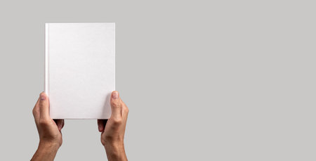 Paper book mockup in men hand on gray banner with copy space. Hardcover mockup, blank empty template, presentation. High quality photoの写真素材