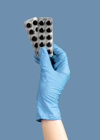 hands in glove holding activated charcoal, black pills.
