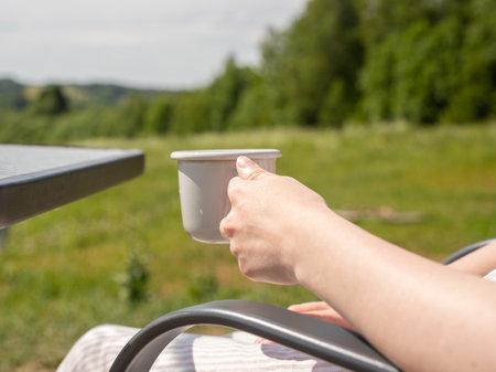 Hand holding tea cup, mug in summer nature, green landscape.の写真素材