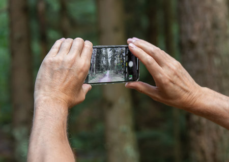 Berlin, Germany July 15 2023 Hands holding phone, taking photo of forest nature.のeditorial素材