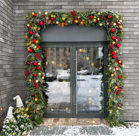 Front door decorated for the Christmas holiday, featuring a festive garland and ornaments. Winter exterior with snow and lights, creating a beautiful entrance for the home.の写真素材