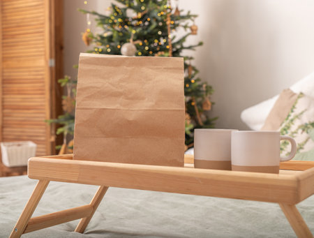 Paper bag and cups on wooden bed tray on Christmas holiday morning. Food delivery mockup.の写真素材