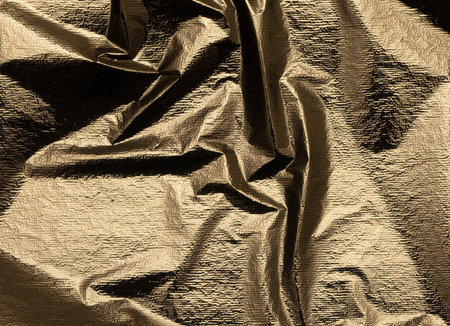 Gold foil fabric background with a sleek, crumpled texture. Shiny, soft surface with elegant folds, reflecting light and creating a warm, metallic glow. Stylish design with a luxurious sheen andの写真素材