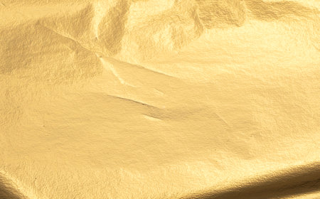 Gold metallic foil texture with a smooth, creased surface. Shiny, reflective material in warm yellow tones, featuring a subtle shimmer and gloss. Elegant design with a gradient effect, rich in detail.の写真素材