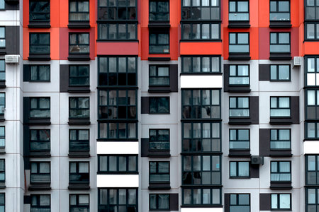 Building with red, black, and white apartment facade in geometric grid pattern. Modern modular structure representing urban housing, minimal style and contemporary residential development.の写真素材