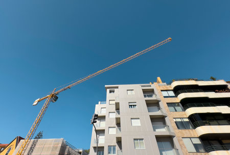 Modern apartment building under construction, with a tall yellow crane stretching across the clear...