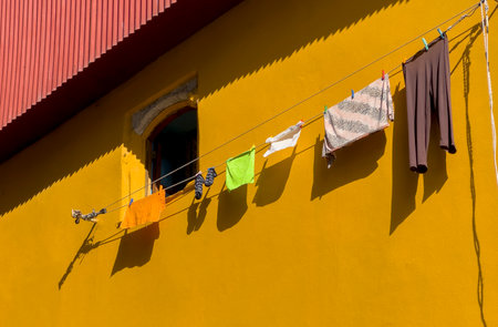 Colorful clothes hanging on a clothesline against a vivid yellow wall with a small window. Urban lifestyle detail from Porto, Portugal, showing laundry drying in the sun.の写真素材