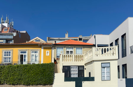 Row of colorful houses with traditional architecture, bright facades, red tiled roofs, and balconies under a clear blue sky. The mix of yellow, cream, and modern white buildings creates a vibrantの写真素材