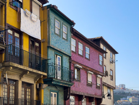 Colorful traditional houses in Porto with tiled facades in yellow, green, and red. Laundry hangs from a balcony, showcasing everyday life in the historic Ribeira district under a clear blue sky.の写真素材