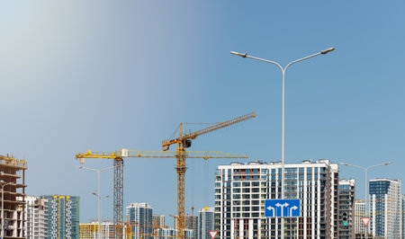Construction cranes over tall unfinished residential and commercial complex with steel framework in metropolitan skyline. Modern multistorey architecture for housing, business, and real estateの写真素材