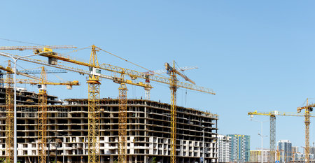 Construction cranes over unfinished highrise condo with concrete framework in metropolitan skyline....