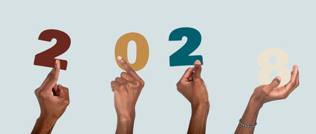 2028 new year celebration scene. African American man with dark skin raising hand and holding colorful number collage, cheerful office team mood, christmas and business typography design background.の写真素材