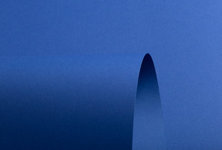 Blue textured paper background with curved cut shape and layered depth. Matte surface with rough...