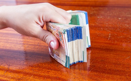 A female hand holding two hundred shekel bank notes against wood background. Concept photo of money,...