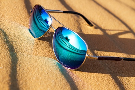 Sunglasses on the sand , summer desert is reflected in the glasses.の写真素材