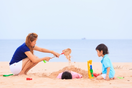 Asian mother and sons playing on sand beachの写真素材